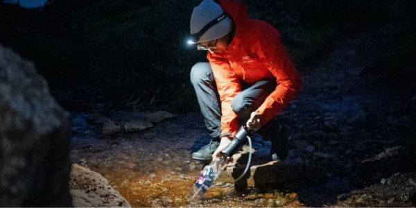 Wasserreinigung Mann filtert Trinkwasser mit Vario Filter Katadyn aus dem Bach Nachts mit Stirnlampe